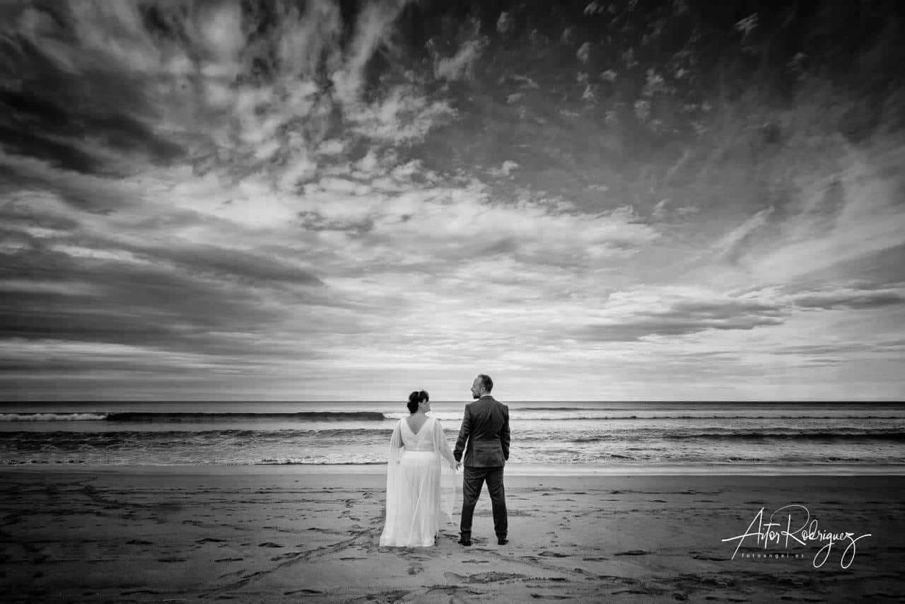 Pareja de recién casados de espaldas en la playa de Zarautz con un cielo dramático, foto de boda en blanco y negro en el País Vasco.